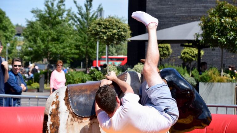 A young man enjoys a thrilling ride on a mechanical bull during a park event in London.
